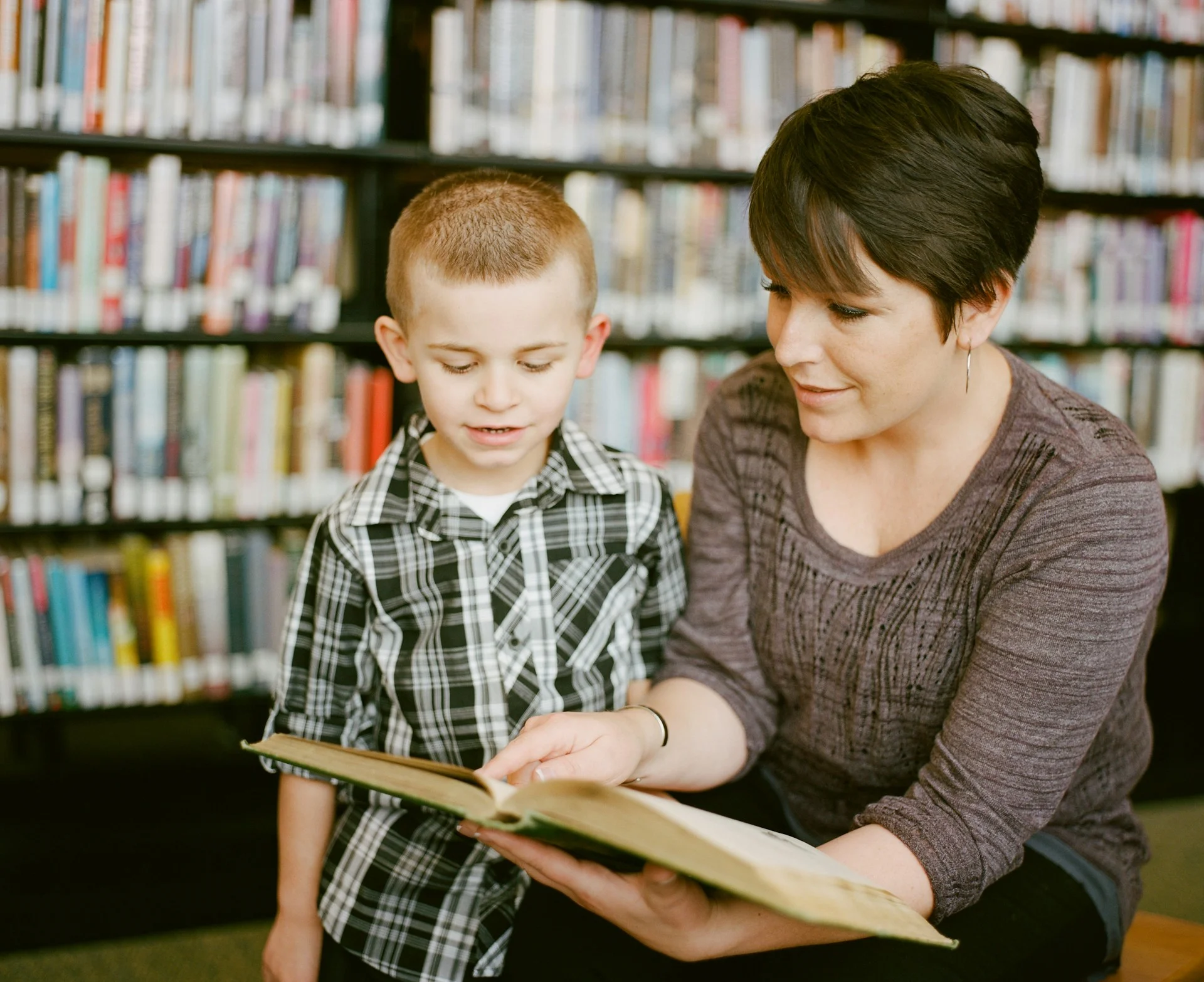 photo - a boy and one of his dyslexia tutors in a library practicing reading