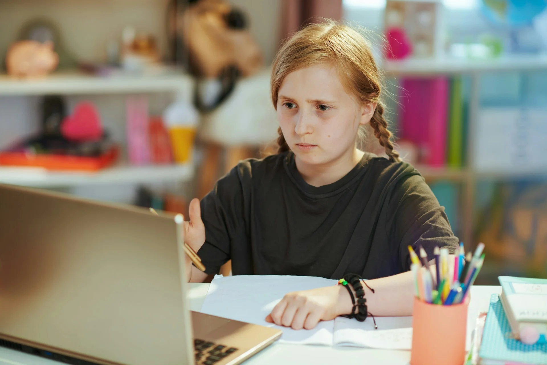 photo - a dyslexic girl looking at her computer screen with books and homework spread out in front of her looking for dyslexia tutors