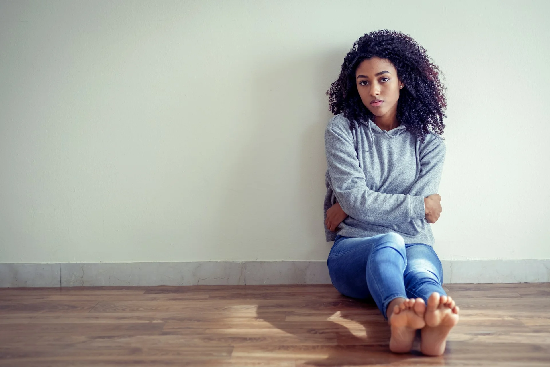 photo - a teenage girl with verbal dyslexia sitting on the floor leaning on the wall with a sad look on her face