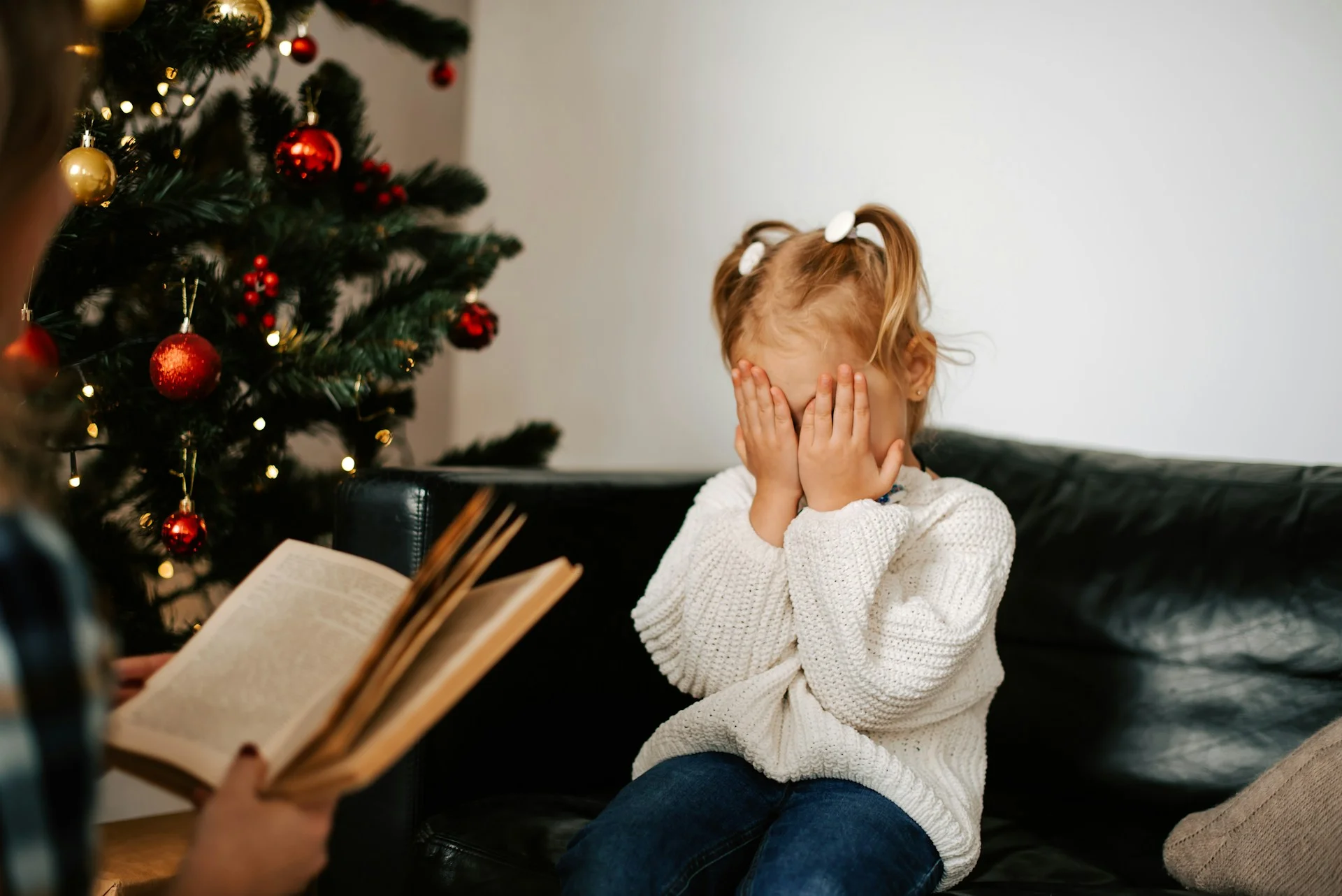 photo - a small girl with dyslexia is sitting on the couch in the living room with her eyes closed and someone reading to her from a book