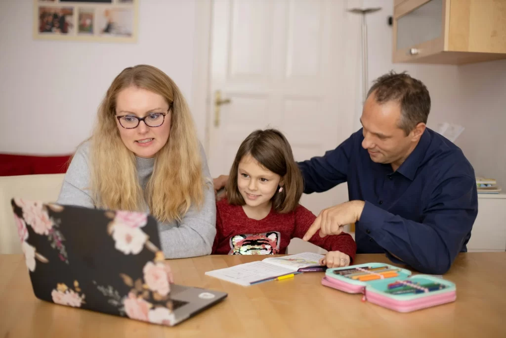 photo - a home schooling tutor and a child with their parent are sitting down and looking at a screen while evaluating home schooling process