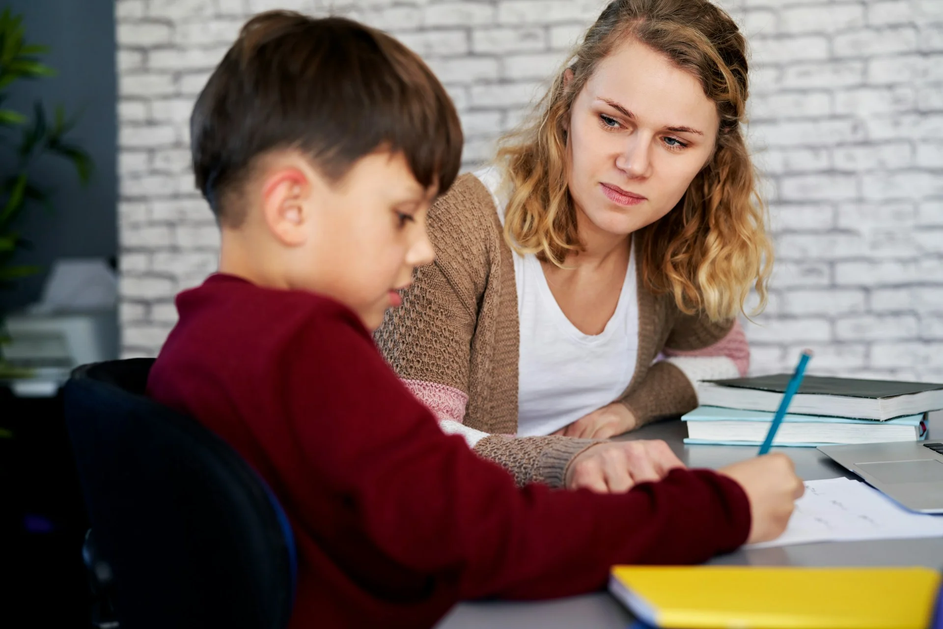 photo - a sen teacher looking at her student during a SEN tutoring session, the young boy drawing on a piece of paper