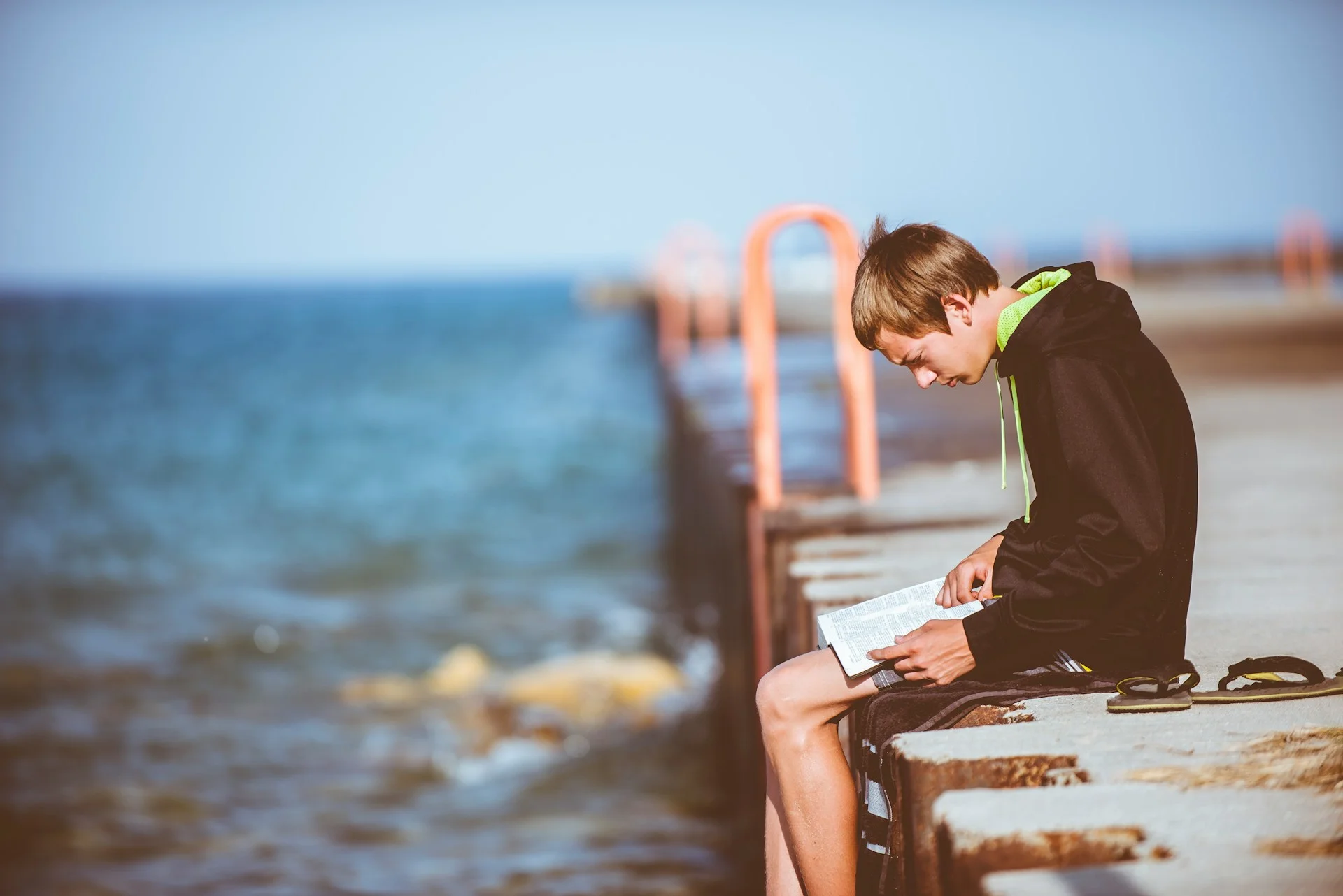 photo - a boy reading about autism and eating disorders on a pier