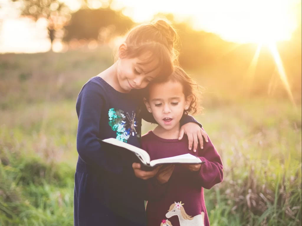 Photo - Two young girls in a field reading a book at special needs schools promoting SEN support in schools 