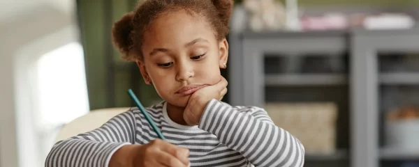 photo - a small girl with ponytails looking at her workbook with SEN or SEND wondering What Does SEND Stand for?